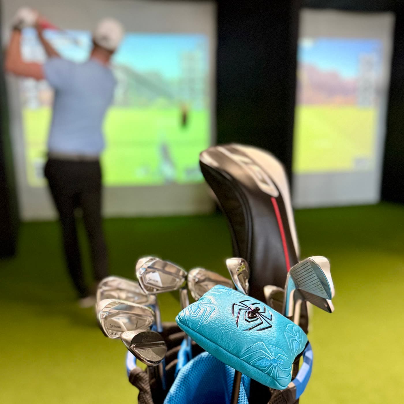 A golfer mid-swing in a simulator bay, club bags in the foreground