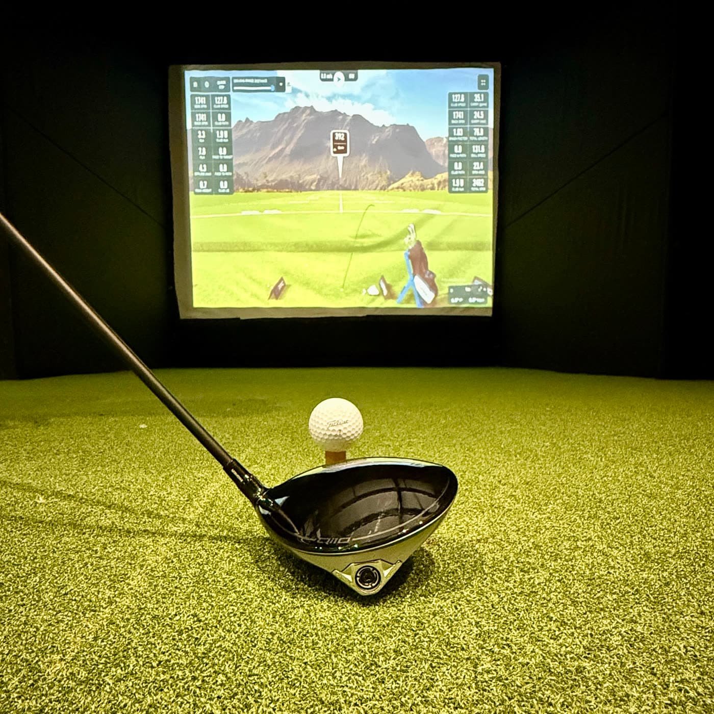 A driver behind a teed ball on the simulator turf, course loaded on the screen